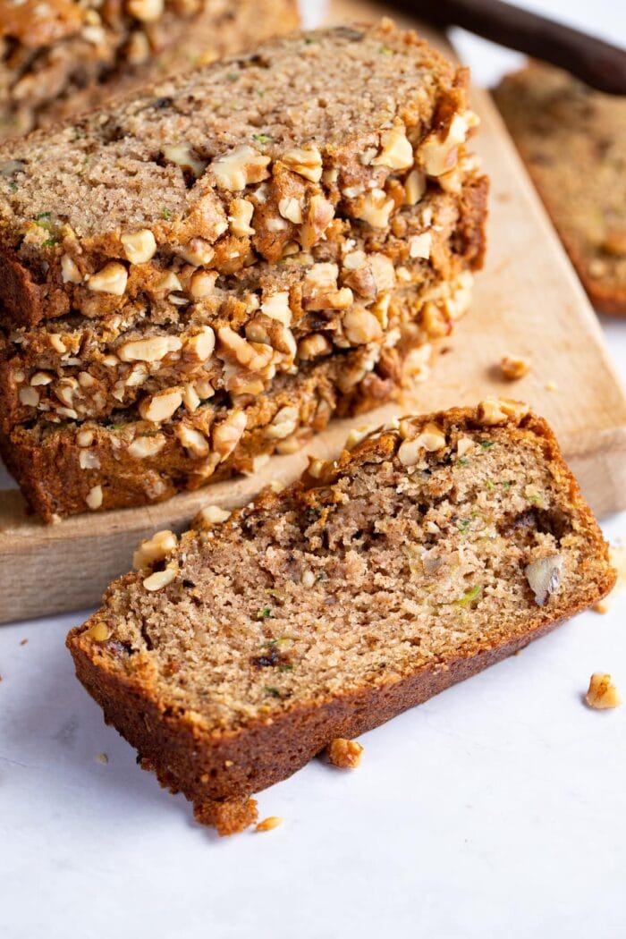 A single slice of vegan zucchini bread in front of a stack of other slices, on light surface