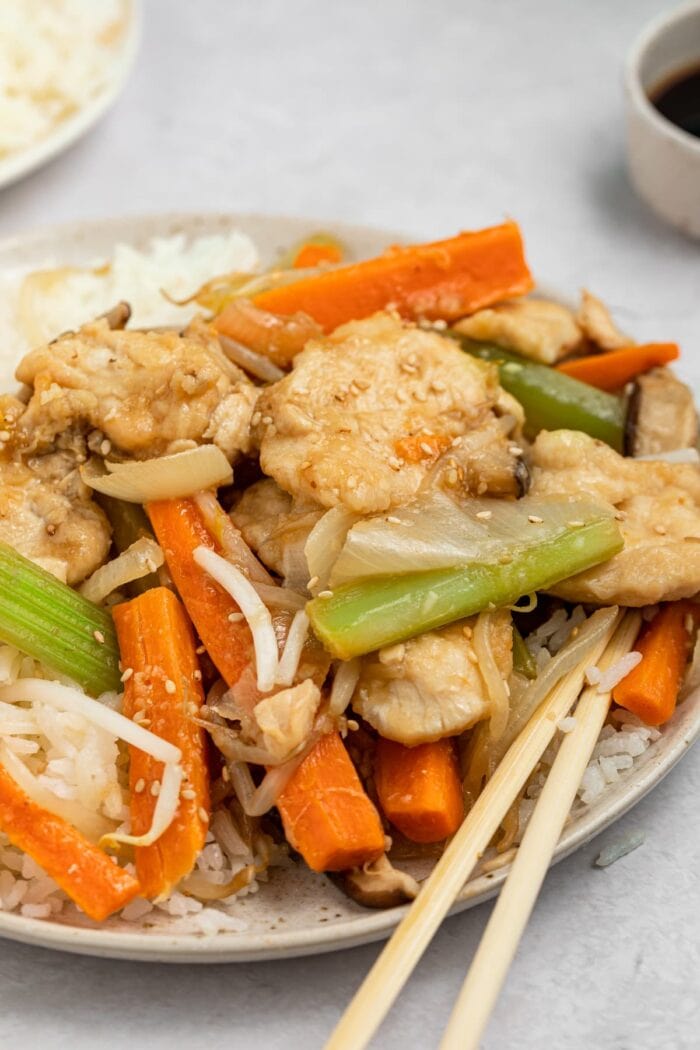 chicken chop suey on a plate with chopsticks and a side of rice