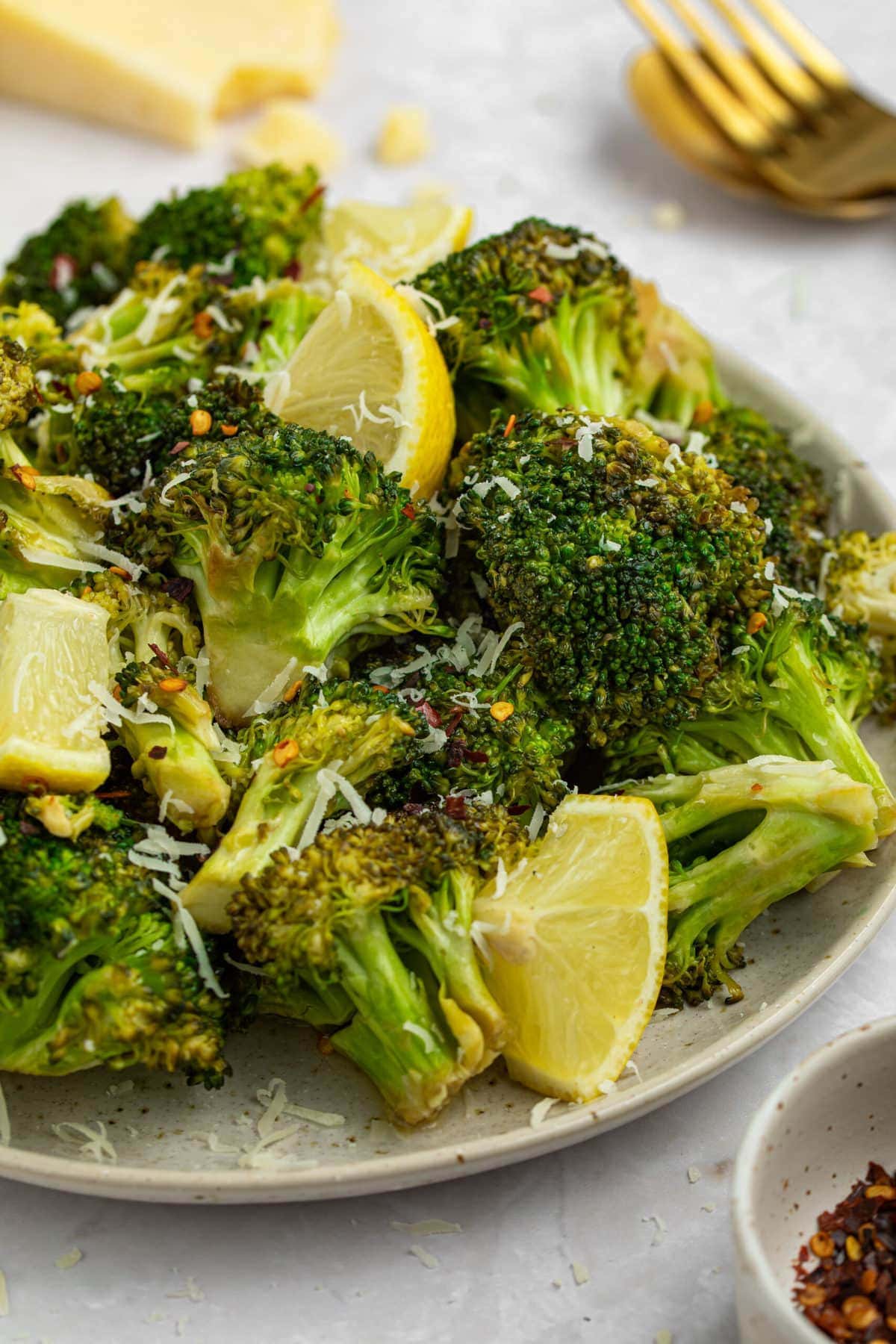 grilled broccoli on a plate with lemon slices and parmesan cheese on the side