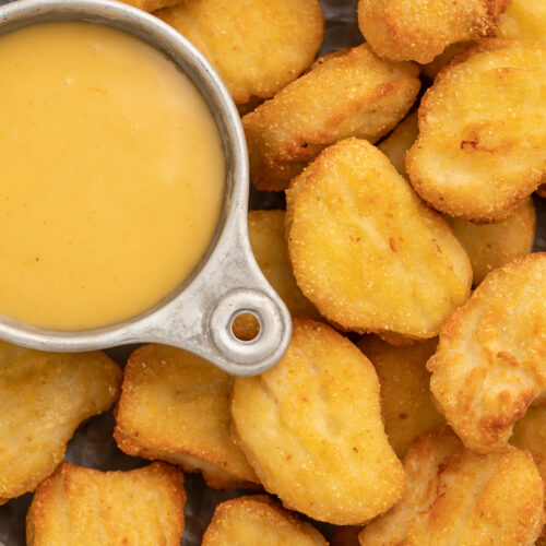 Close-up of air fryer frozen chicken nuggets in a large bowl, next to a small dipping bowl filled with honey mustard sauce.