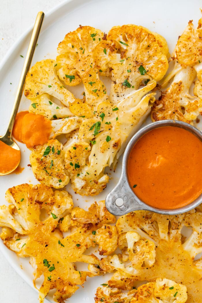 Zoomed out shot of two cauliflower steaks next to a small dipping bowl of romesco sauce