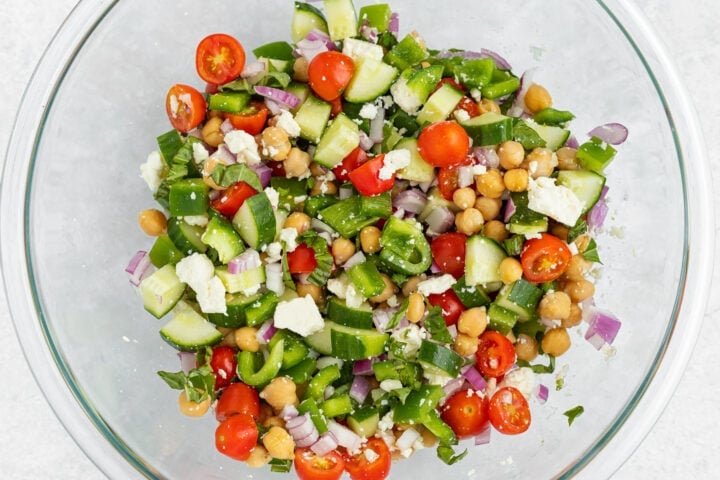 Ingredients for Mediterranean chickpea salad in a large glass mixing bowl, before dressing is added.