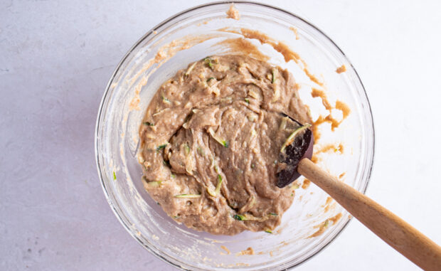 Grated zucchini folded into gluten free zucchini bread batter in large glass mixing bowl