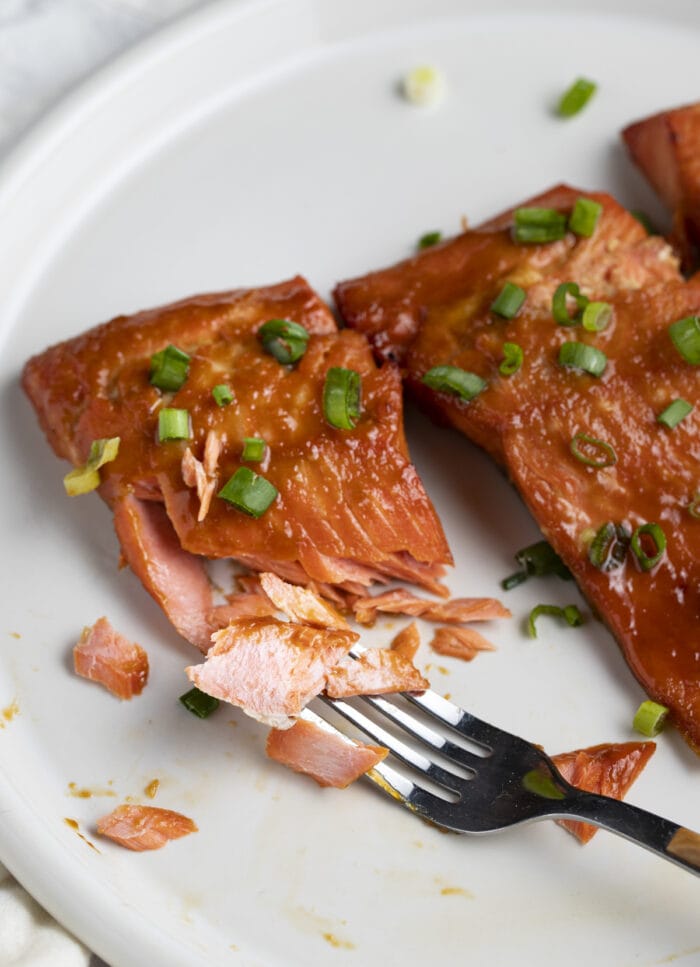 Miso salmon fillets on a white plate. The focus is on a fillet that has been cut with a fork to show the flaky interior meat