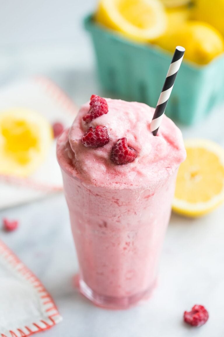 Paleo raspberry frosted lemonade in a glass with a black and white straw and lemons in the background