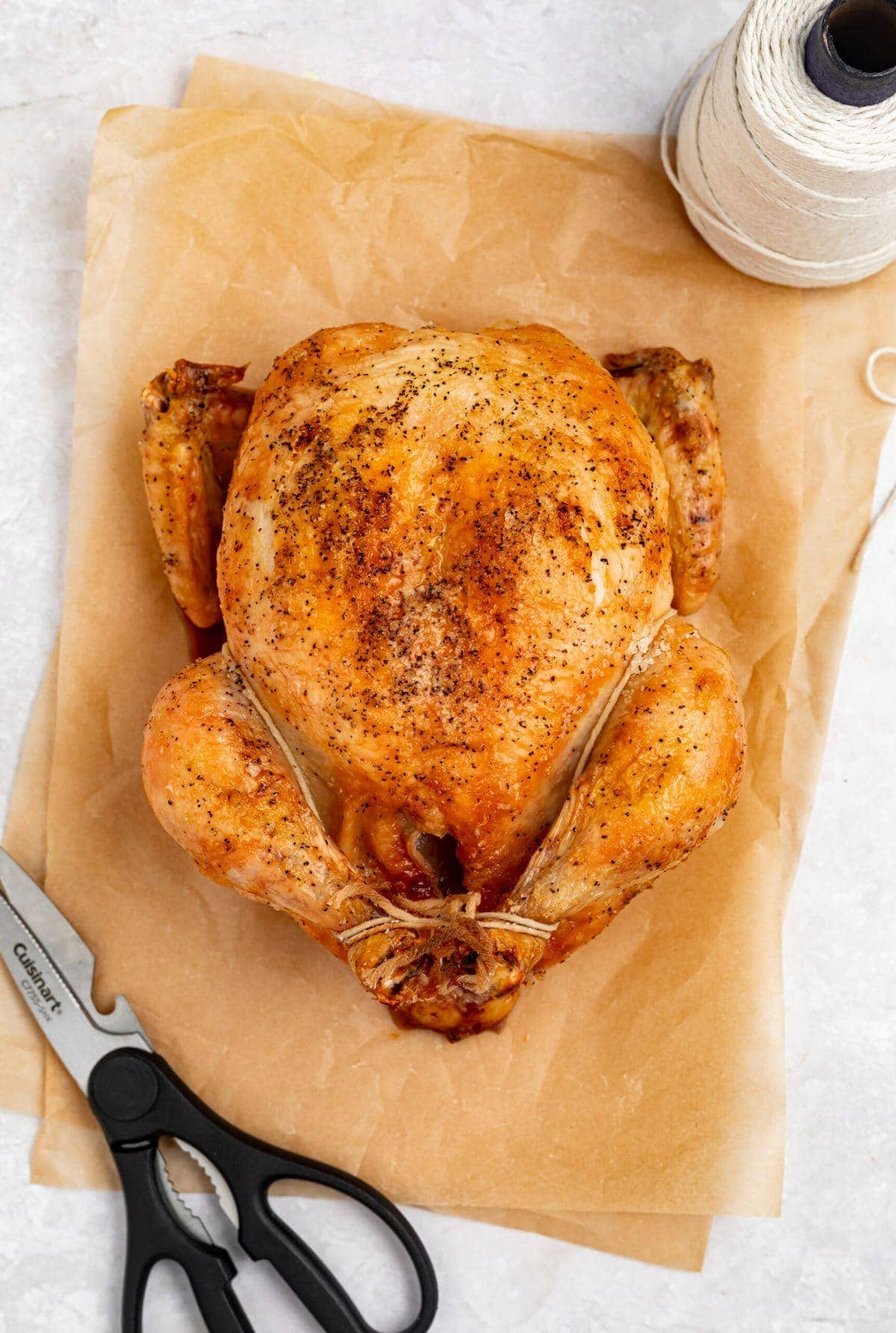 showing how to truss a chicken on two sheets of parchment paper with scissors and butcher's twine