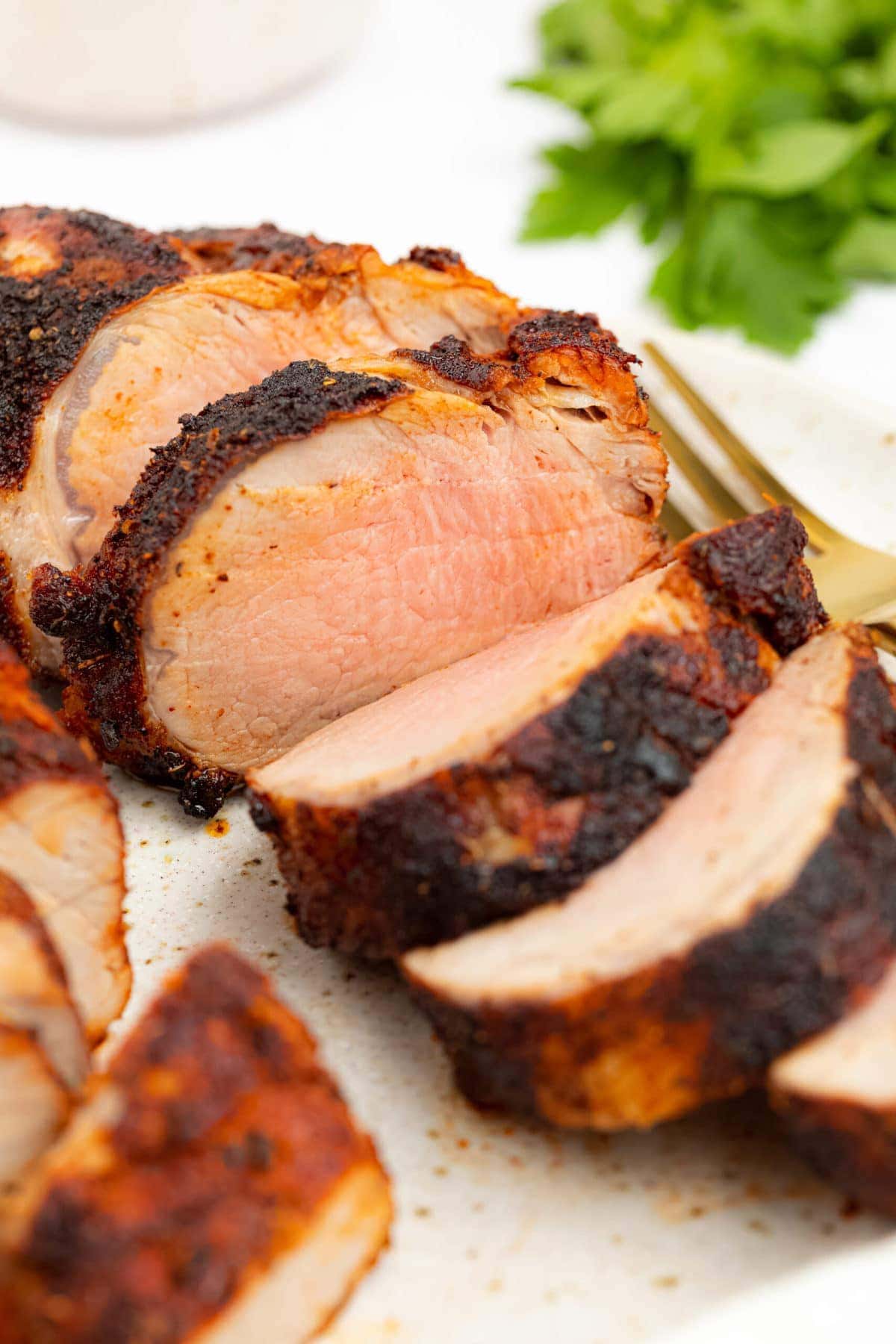 air fryer pork tenderloin on a plate with a fork and fresh parsley on the side