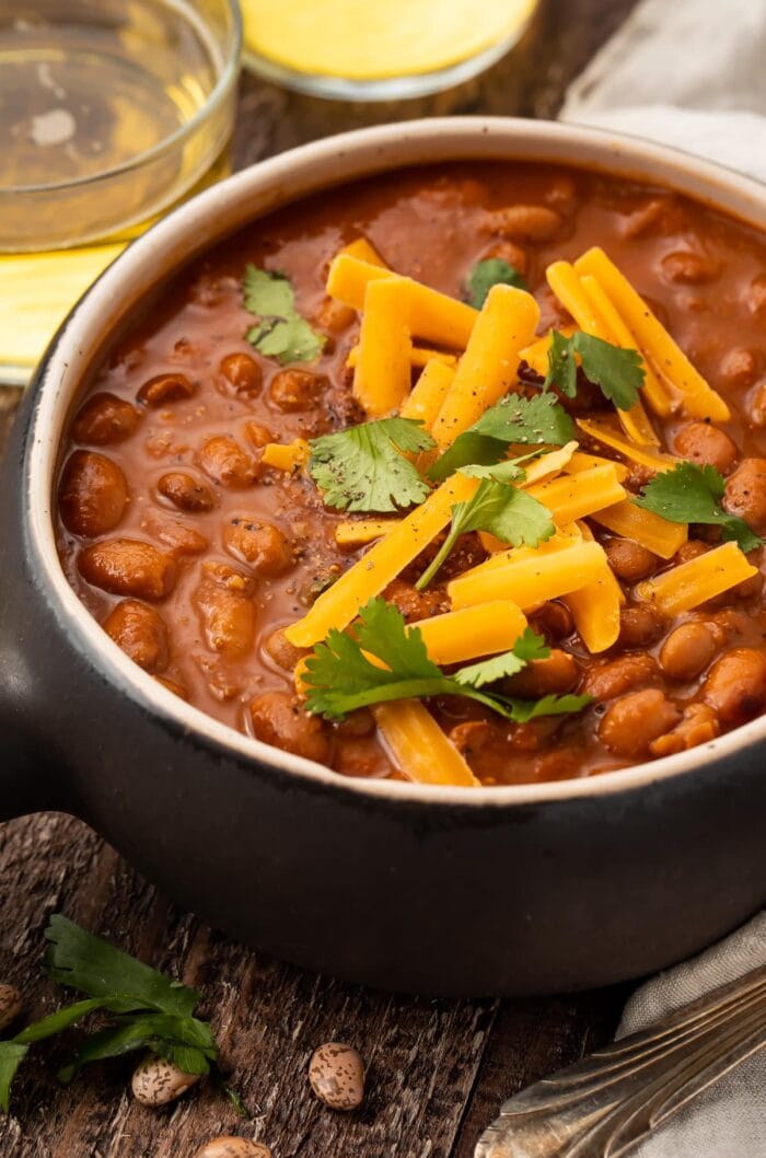 Angled photo of ranch style beans topped with shredded cheese and green onions in a small black bowl