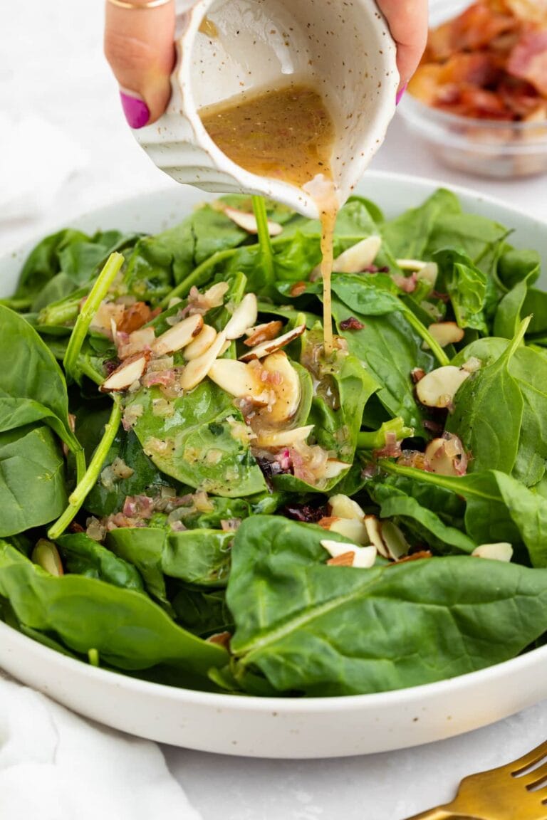 hot bacon dressing being poured over spinach salad