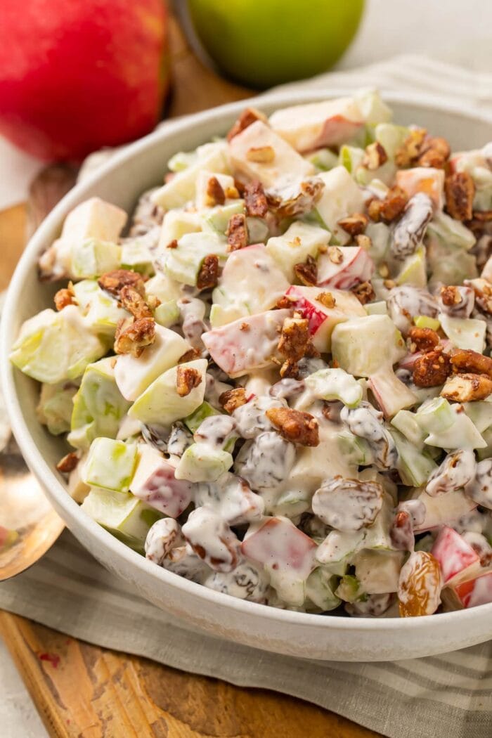 Slightly zoomed out shot of apple salad in a large bowl, with whole apples in the background