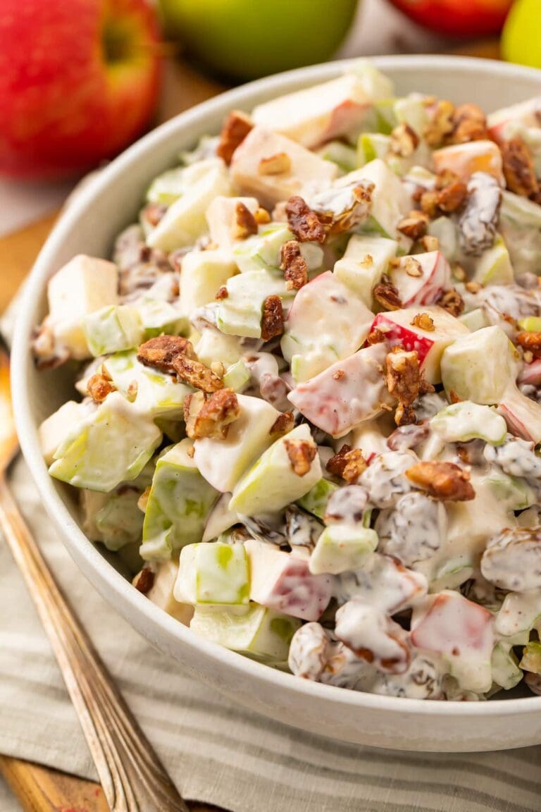 Close up, slightly overhead angle of apple salad in a large bowl, with whole apples in the background