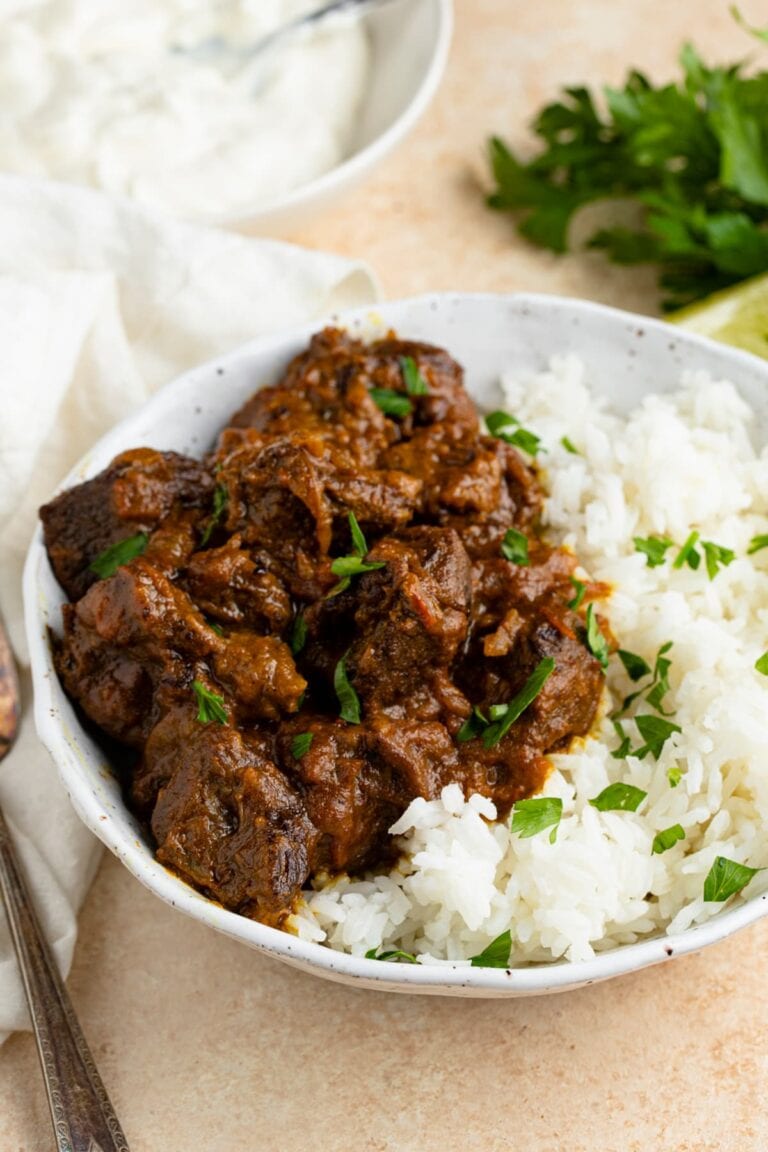 Beef curry in a white speckled bowl with white rice, garnished with parsley