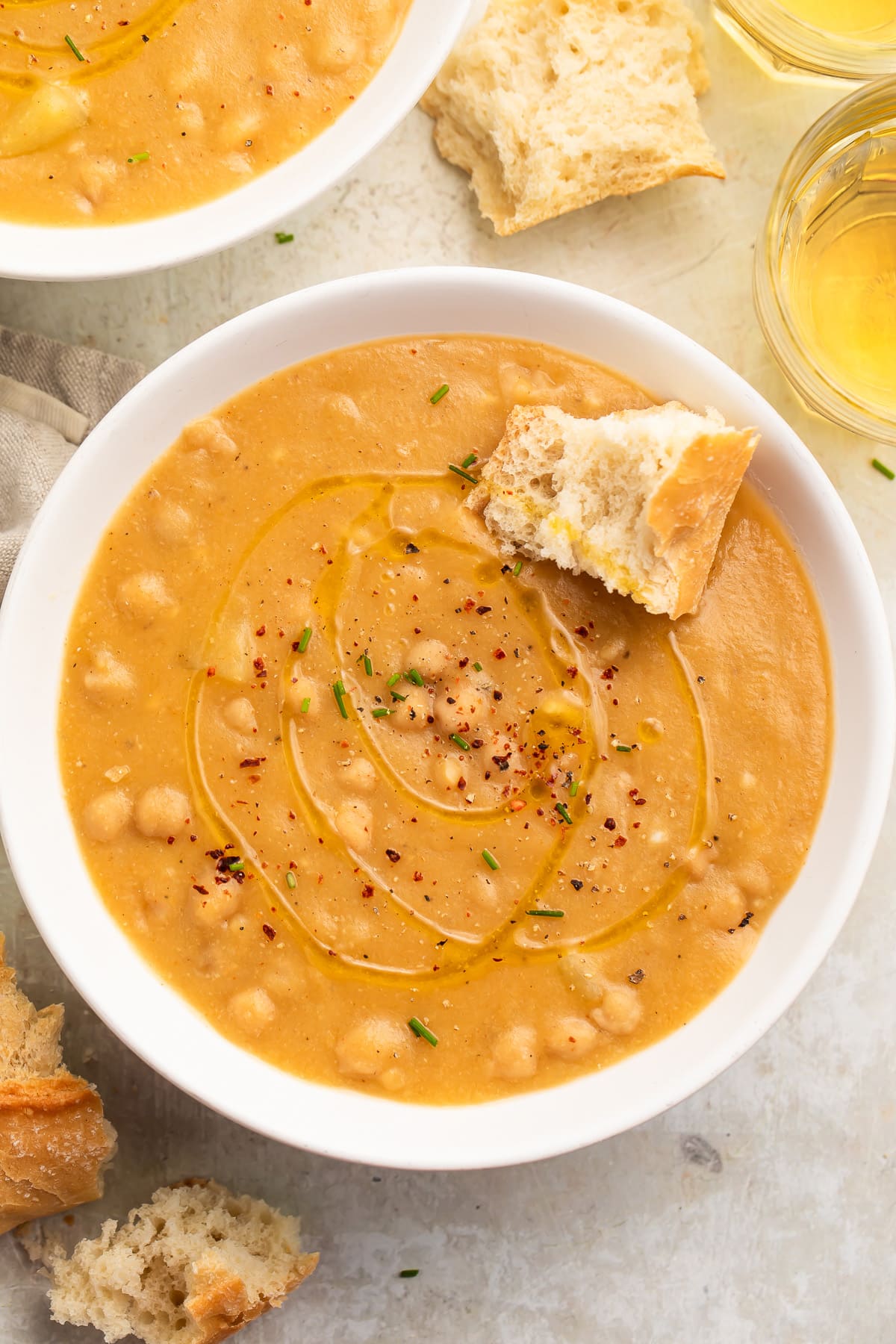 Top-down view of a white soup bowl holding creamy, golden chickpea soup with a piece of crusty bread resting in the soup.