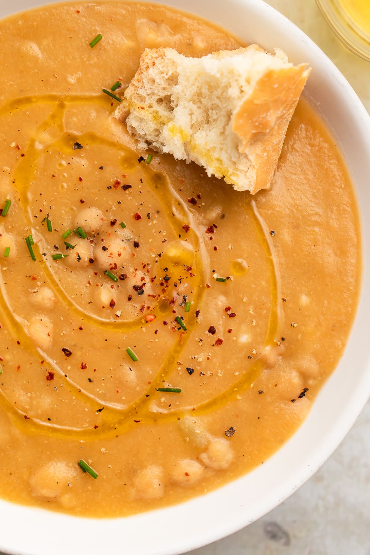 Top-down close-up of a white soup bowl holding creamy, golden chickpea soup with a piece of crusty bread resting in the soup.