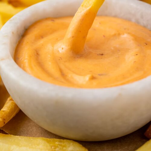 A french fry dipped into a small bowl of chipotle mayo