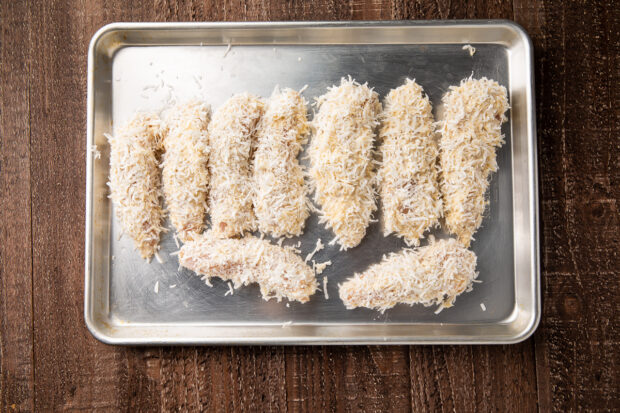 Battered coconut chicken strips on baking sheet