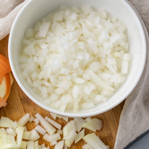 Diced onion on a cutting board next to a bowl of diced onion