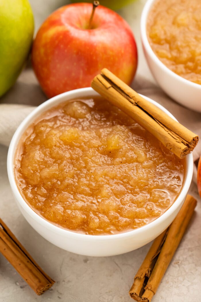 Instant Pot applesauce in a large bowl surrounded by apples and topped with a whole cinnamon stick