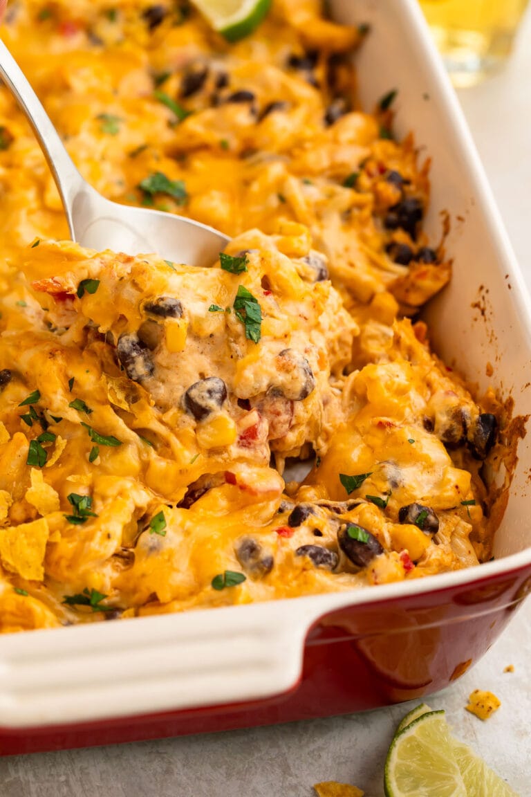 A spoonful of Mexican chicken casserole being lifted out of a large casserole dish.