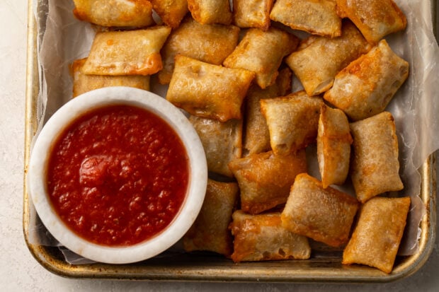 Pizza rolls cooked in the air fryer on a plate with a bowl of pizza sauce