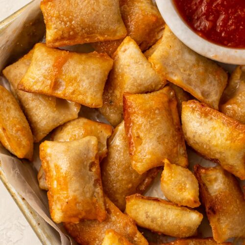 Pizza rolls cooked in the air fryer on a plate with a bowl of pizza sauce