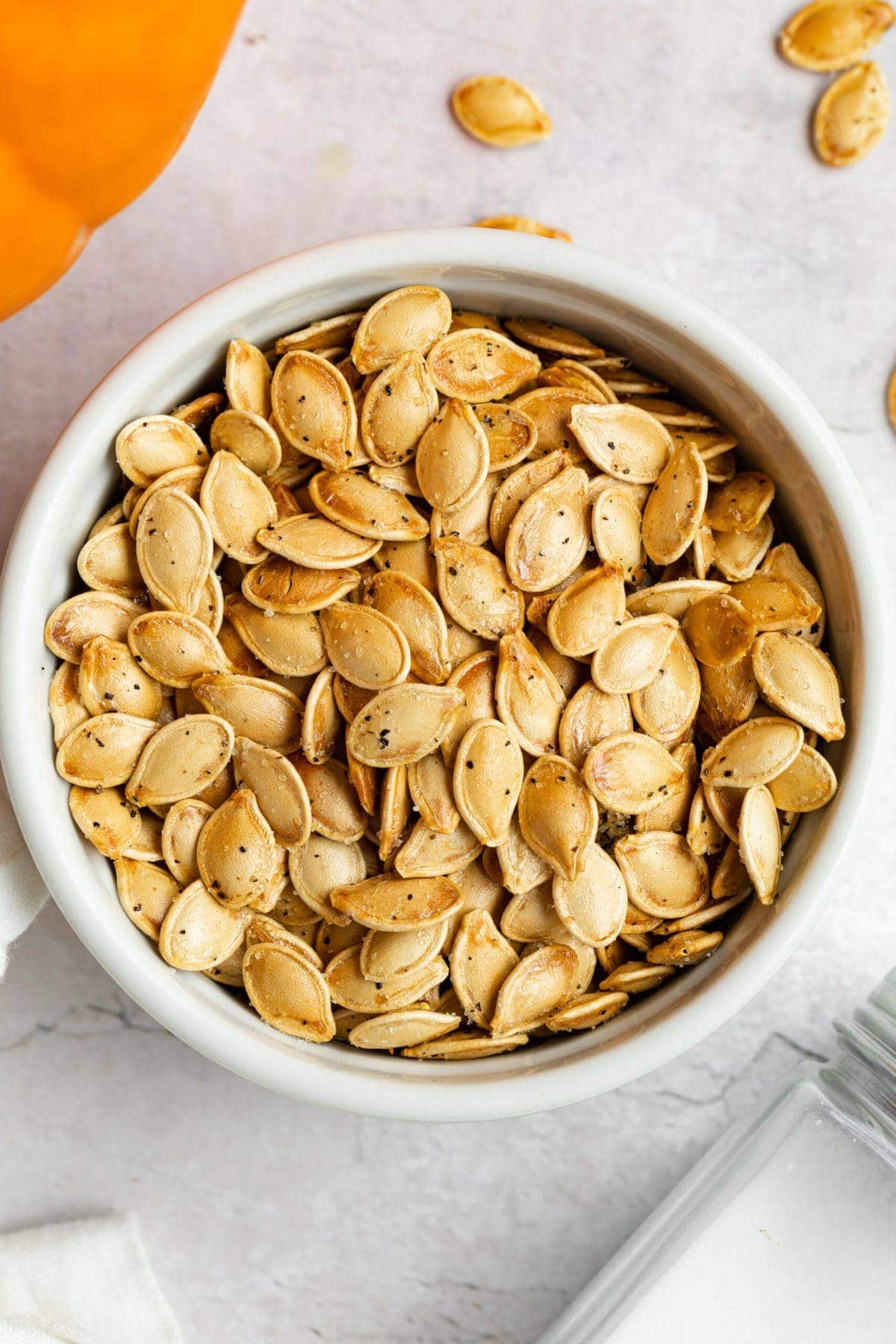 air fryer pumpkin seeds in a dish with a pumpkin on the side