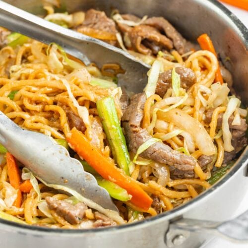 beef chow mein in a skillet with tongs