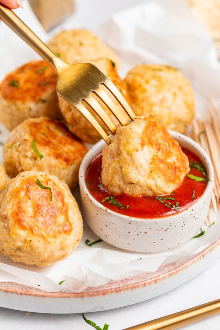 baked chicken meatballs being dipped into tomato sauce