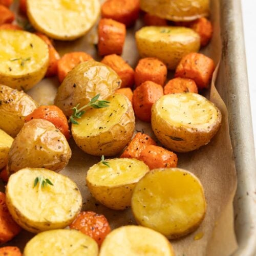 roasted potatoes and carrots on a baking sheet with fresh thyme on top