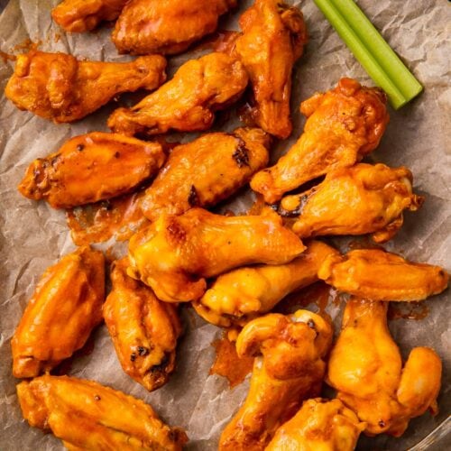 Air fryer frozen chicken wings on a baking sheet with parchment paper and celery sticks