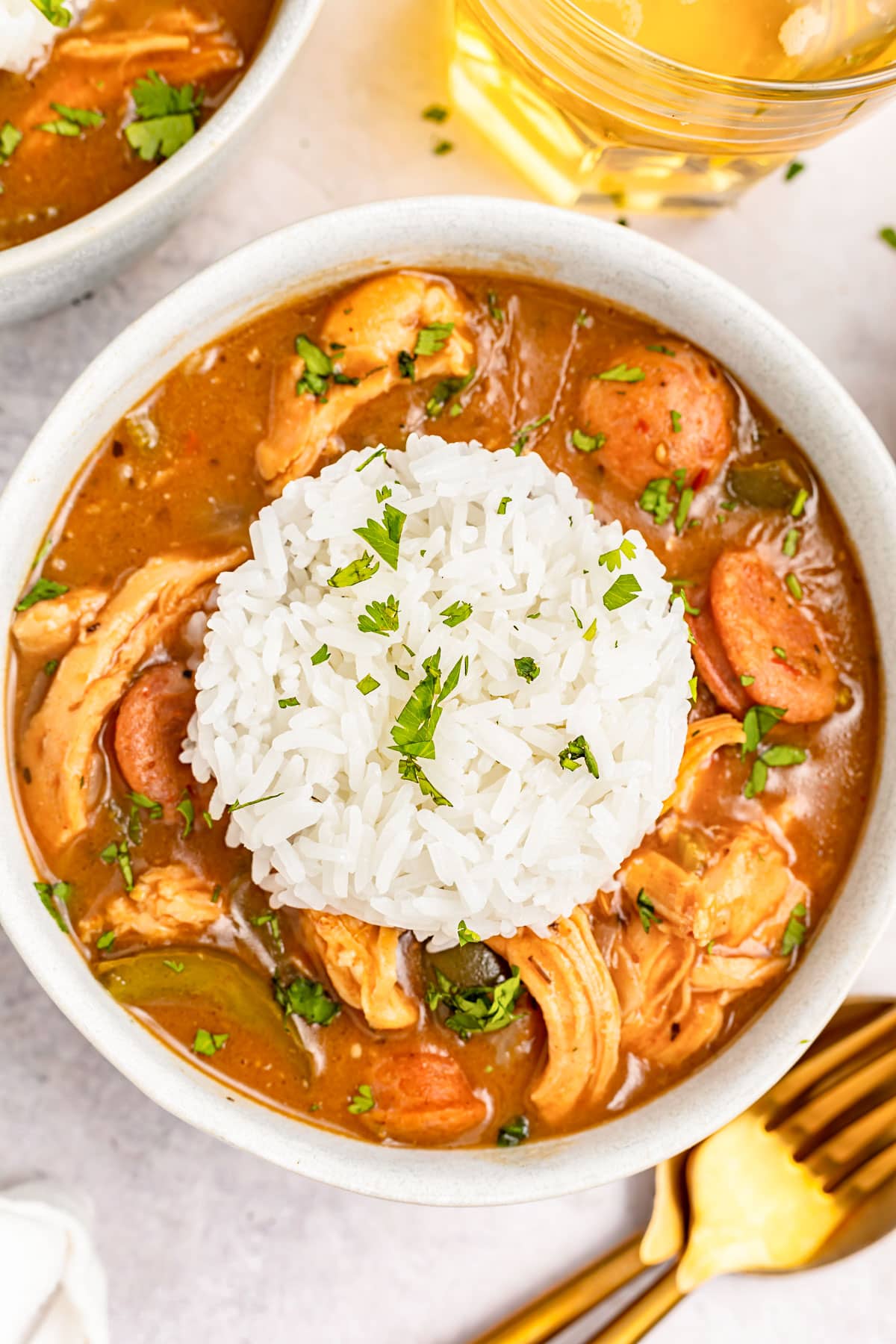 Overhead image of a white bowl holding deep reddish brown chicken an sausage gumbo with a mound of white rice in the center.