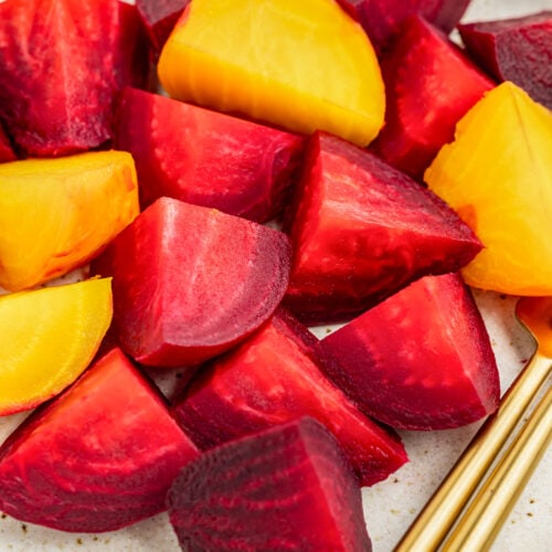 Zoomed out view of chunks of red and golden beets on a white plate with gold silverware.