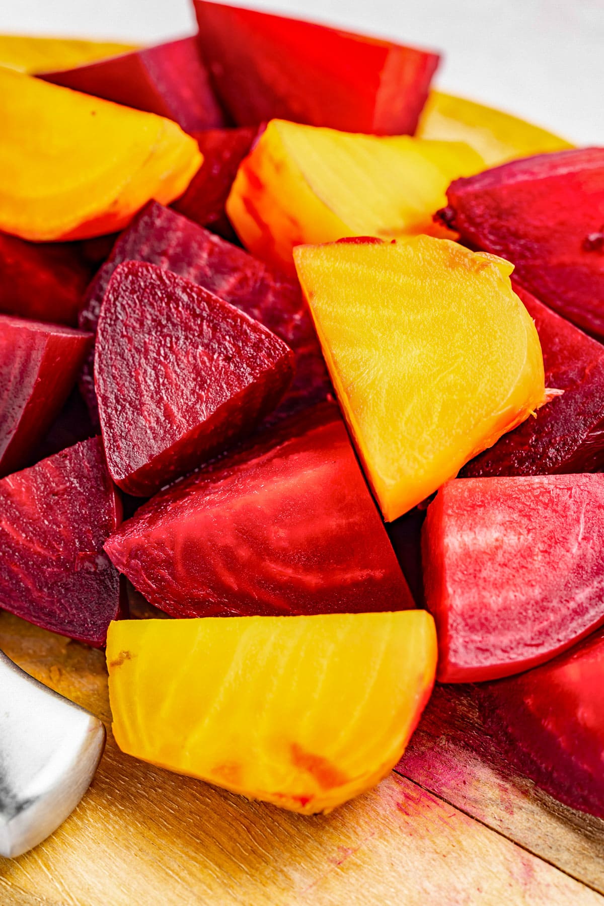 Large chunks of red and yellow beets on a wooden cutting board.