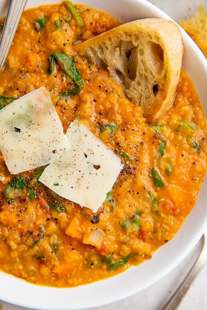 Close up of a bowl of Instant Pot lentil soup, crusty bread, and parmesan cheese