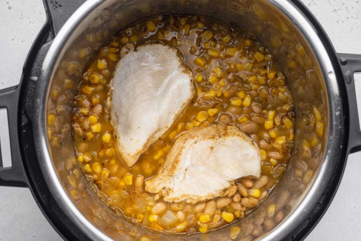 Chicken on top of a bed of ingredients for white chicken chili in the Instant Pot.