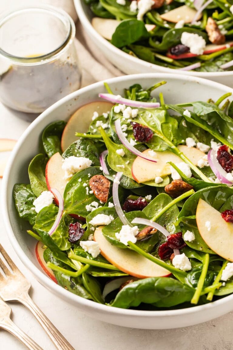 Spinach salad in a large bowl with another bowl of spinach salad in the background