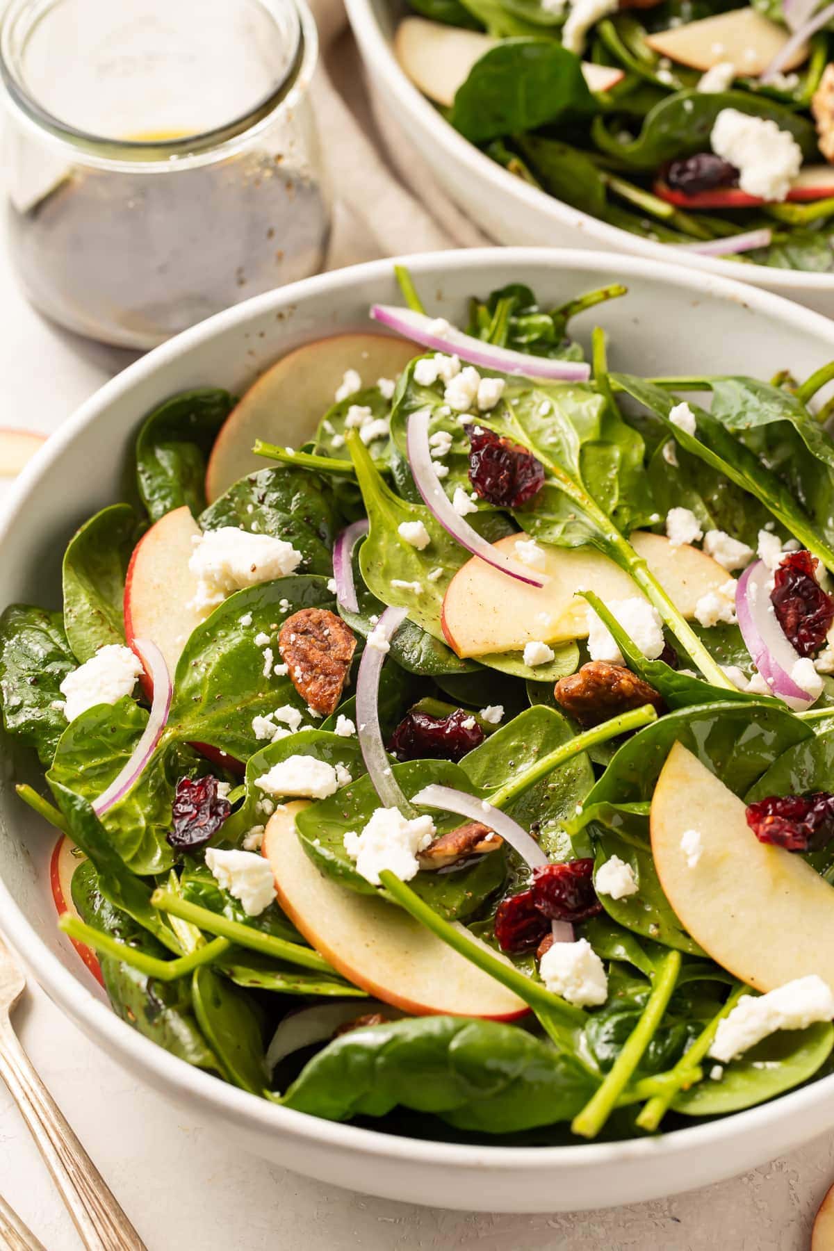 Spinach salad in a large bowl with another bowl of spinach salad in the background.