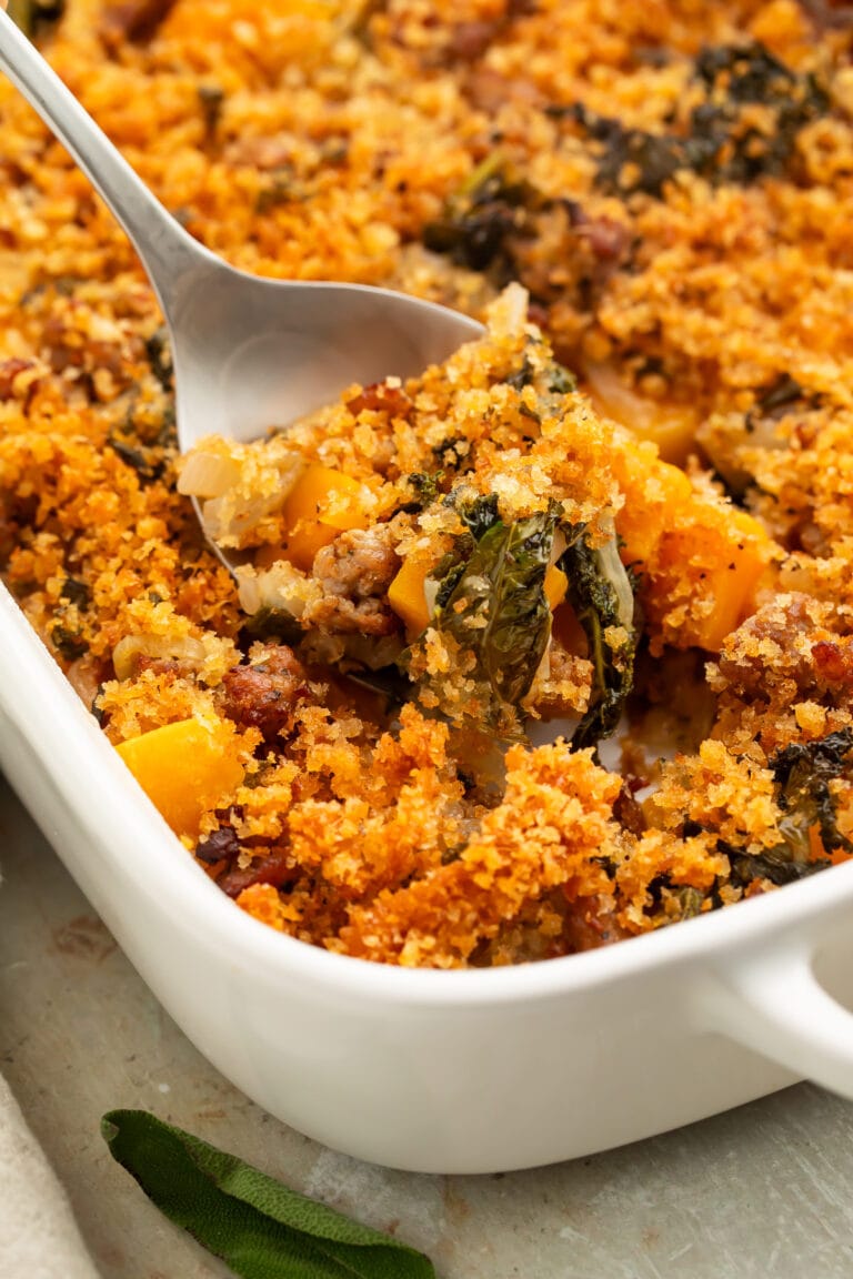 A scoop of butternut squash casserole being lifted out of a casserole dish with a large silver spoon.