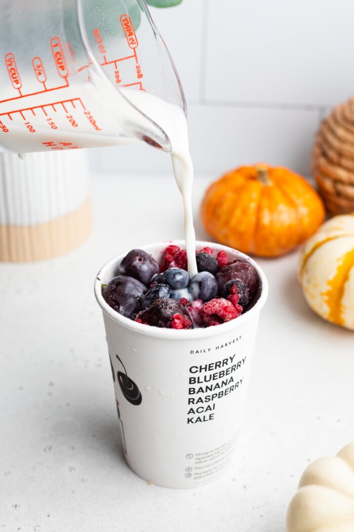 Milk poured into a smoothie cup of berries