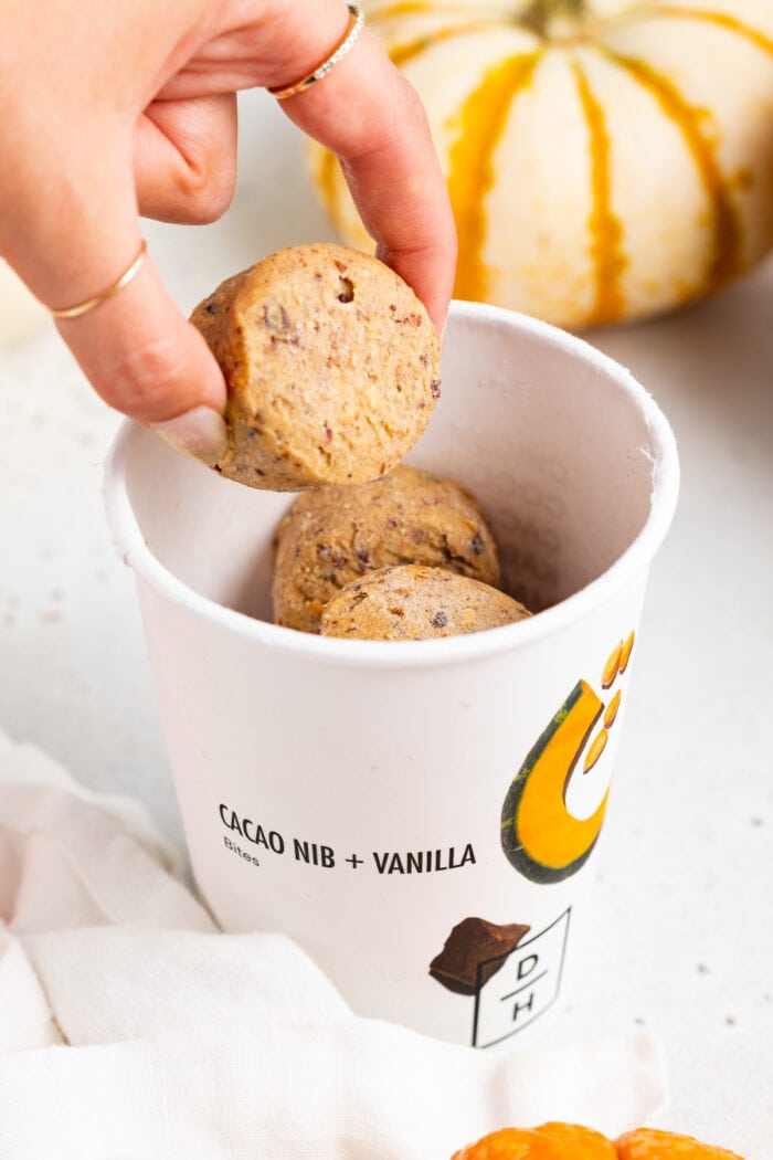 Daily Harvest bites in a paper cup. A hand picks up one bite out of the cup