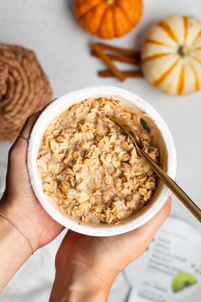 Daily Harvest oat bowl held in two hands over a white tabletop with pumpkins in the background