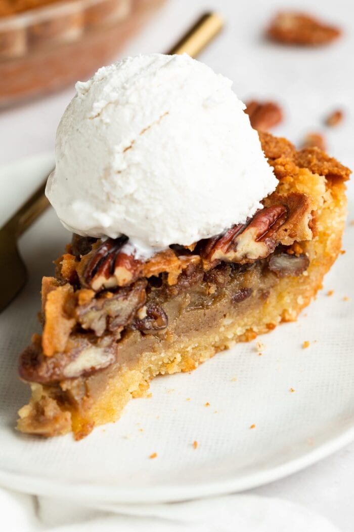 slice of keto pecan pie on a plate with sugar-free vanilla ice cream on top