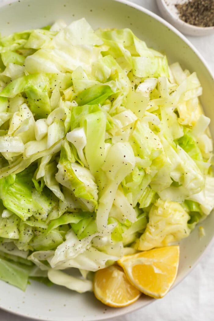 sauteed cabbage in a bowl with fresh lemon sliced and black pepper on the side