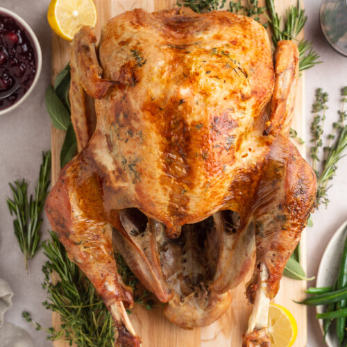 Overhead view of a whole sous vide turkey on a serving board garnished with fresh green herbs and lemon slices.