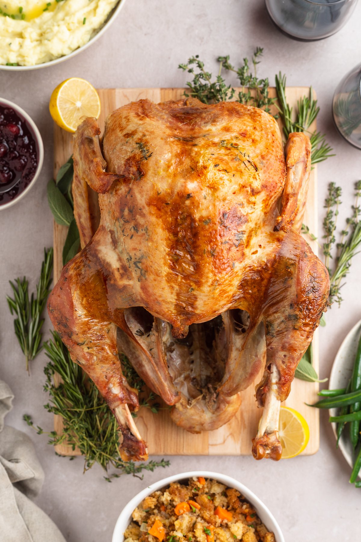 Overhead view of a whole sous vide turkey on a serving board garnished with fresh green herbs and lemon slices.