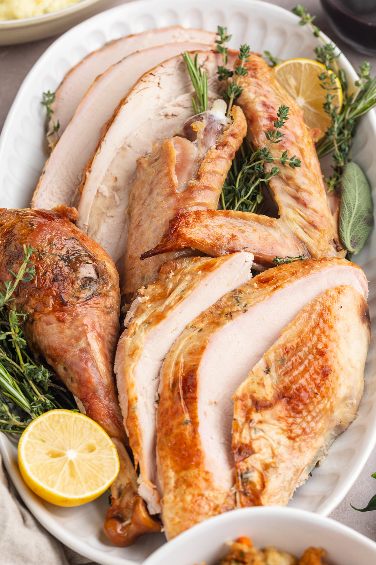 A closer look at a sous vide turkey, carved into thick slices then placed on a serving platter with green herb garnish and lemon slices.