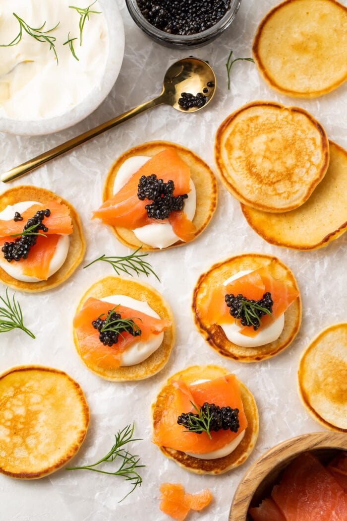 Blini, some topped with salmon and caviar, spread out on a table