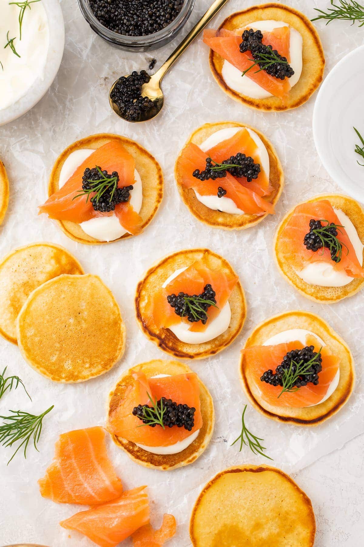 Blini, some topped with salmon and caviar, spread out on a table