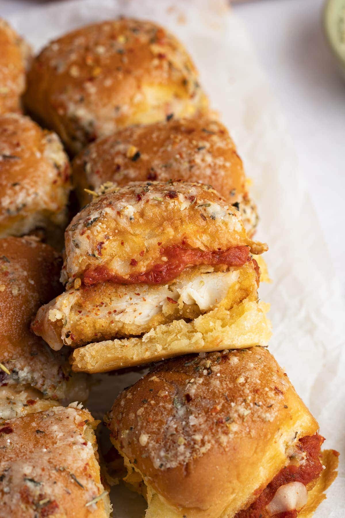 Crispy chicken parm sliders, with one slider laying on top of the others at an angle to show chicken and marinara inside