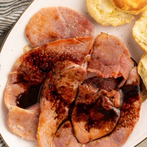 Red eye gravy poured over country ham on an oval platter with fluffy biscuits.